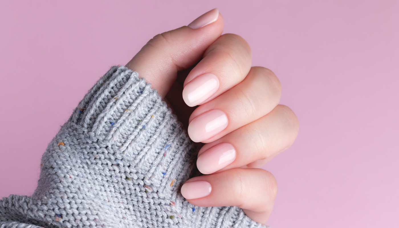 A beautiful pink manicure on the nail salon menu, with soft pink background and sweater sleeve – a simple example of manicure and pedicure services