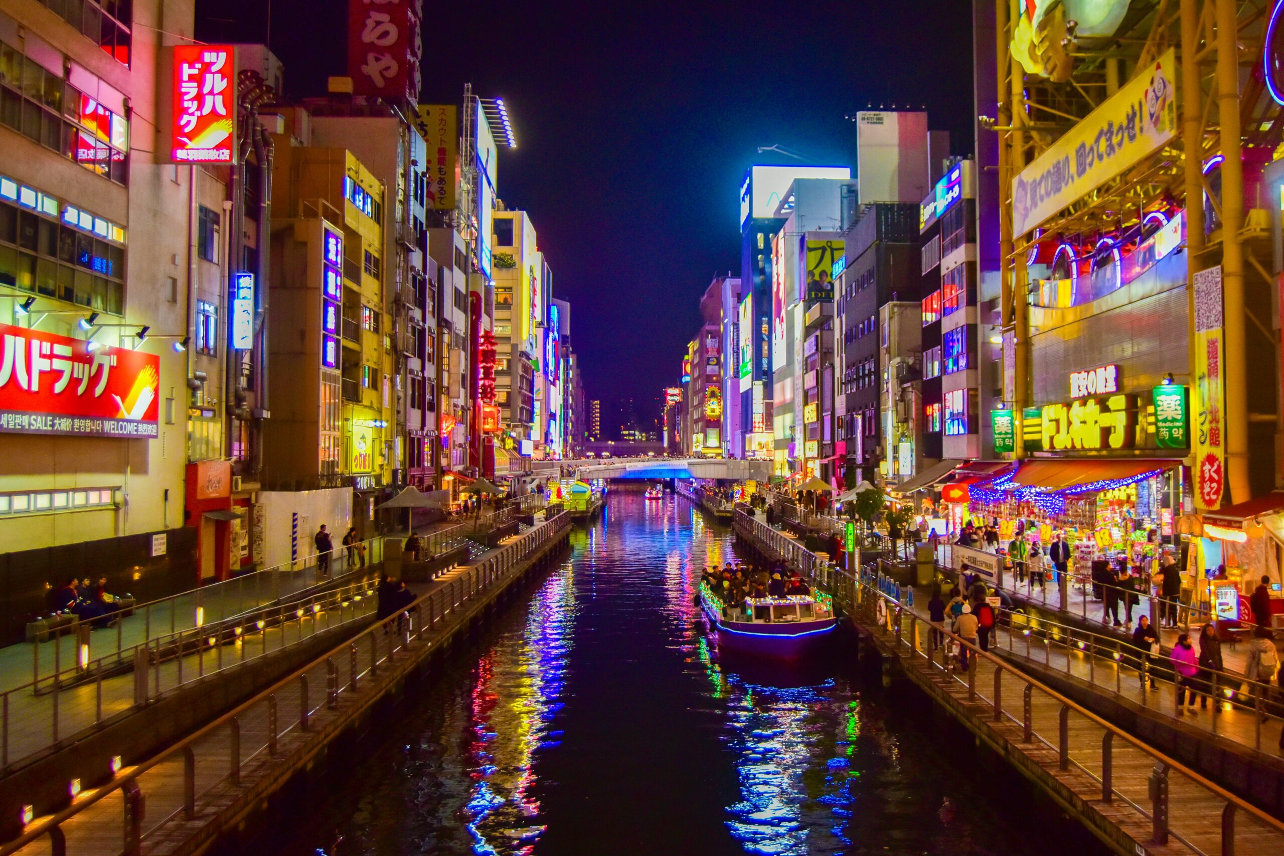 Busy riverside area in Osaka at night with people walking and lights reflected on the water